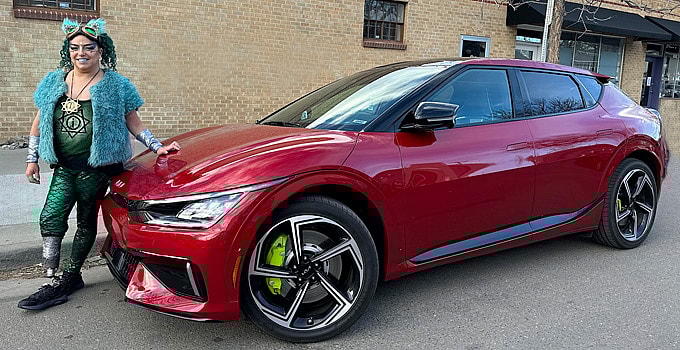 Leg amputee woman, dressed in colorful clothes, leans against the Kia EV6 GT