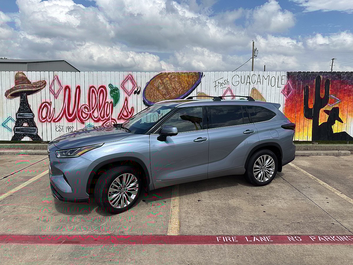 A 2024 Toyota Highlander Hybrid parked in front of tasteful Texican graffiti most affordable 3 row SUVs