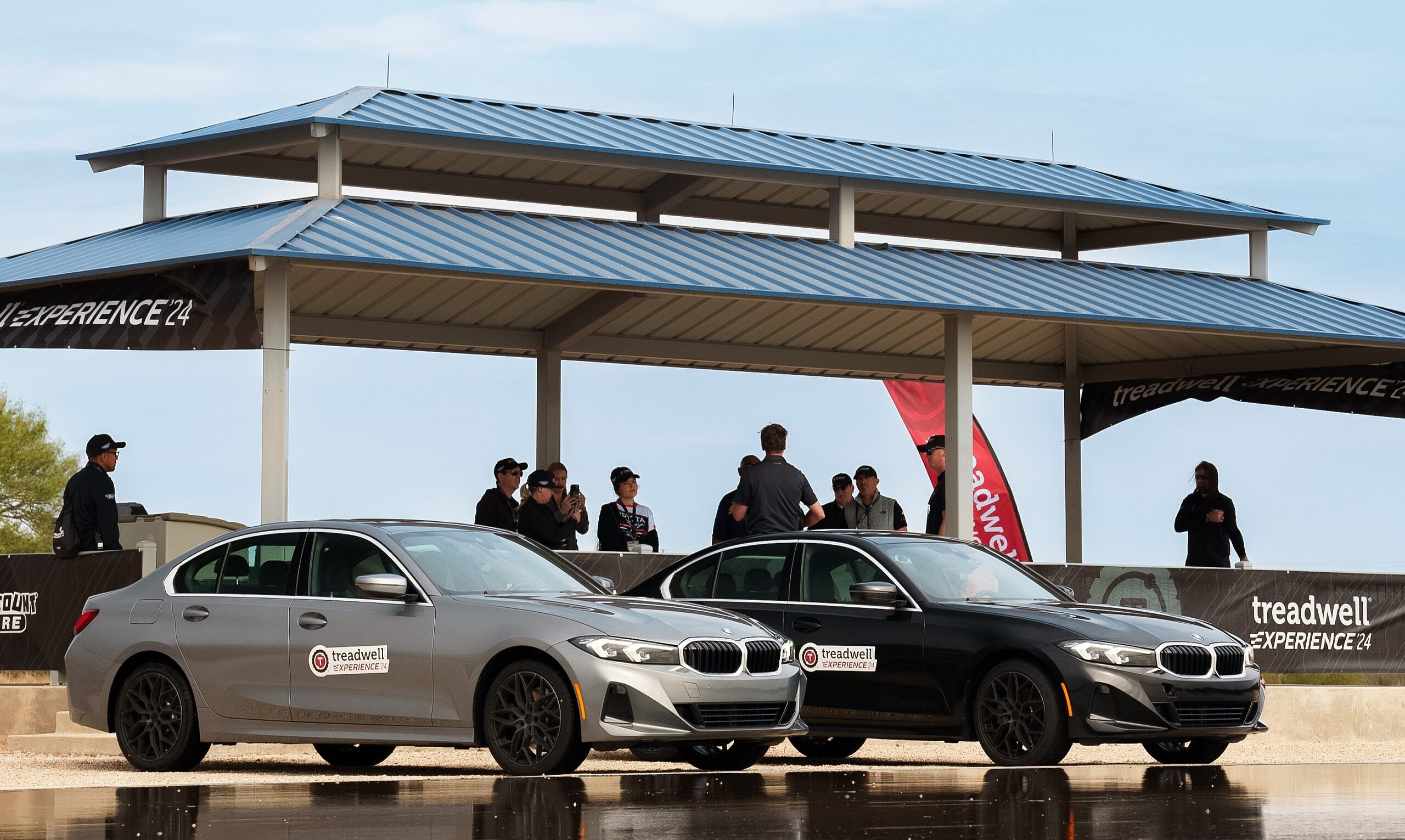 Two BMW 3-Series equipped with two different types of tires lining up to be tested on a wet surface
