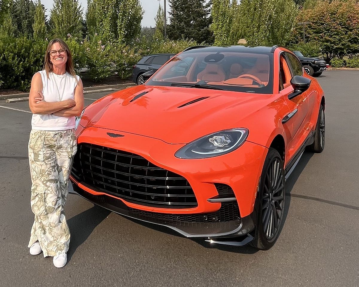 Sara Lacey standing in front of an Aston Martin SUV in bright orange at the Heels and Wheels event in Portland, OR