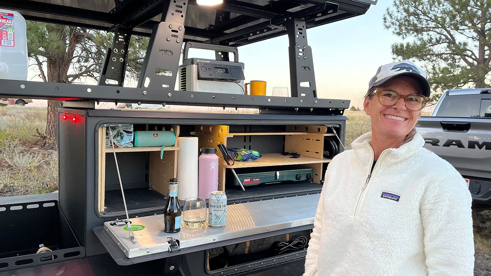 A Woman Smiling While Standing Next To A Camping Trailer, Showcasing The Storage Capacity Of The Taxa Woolly Bear Camping Trailer