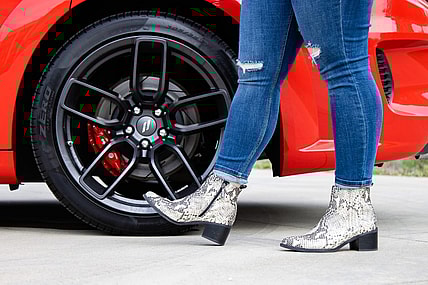 A Woman Wearing Snakeskin Boots Standing Next To The Wheels Of A Dodge Challenger Car Core
