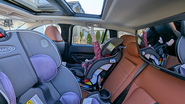 Car Seats Installed In The 2025 Mazda Cx-50 2.5 Turbo Premium Plus, With A Toddler Reaching Toward The Large Sunroof