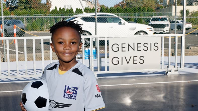 A New Soccer Field Is Driving Change Thanks to ... Genesis? Here's How the Company Is Giving Back 1 A Young Athlete Stands In Front Of A Sign Reading &Quot;Genesis Gives&Quot; While Holding A Soccer Ball And Smiling
