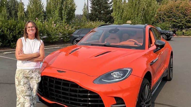 Sara Lacey Standing In Front Of An Aston Martin Suv In Bright Orange At The Heels And Wheels Event In Portland, Or