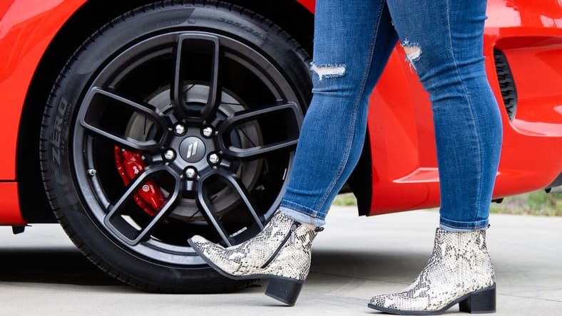 A Woman Wearing Snakeskin Boots Standing Next To The Wheels Of A Dodge Challenger Car Core