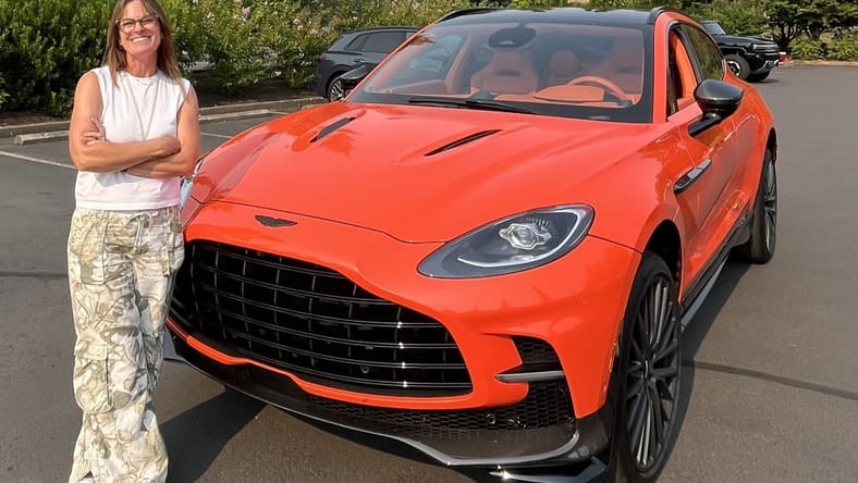 When 25 Women Test Drive Dream Cars, What Do They Choose? You Might Be Surprised. 2 Sara Lacey Standing In Front Of An Aston Martin Suv In Bright Orange At The Heels And Wheels Event In Portland, Or