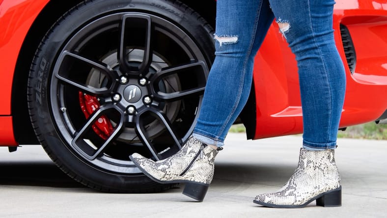 A Woman Wearing Snakeskin Boots Standing Next To The Wheels Of A Dodge Challenger Car Core