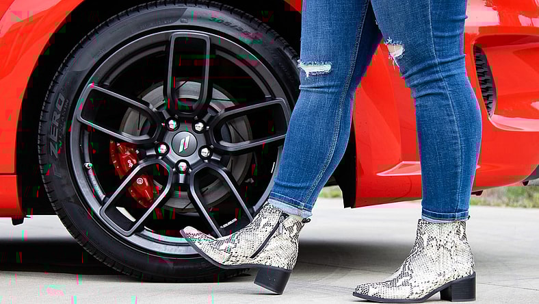 A Woman Wearing Snakeskin Boots Standing Next To The Wheels Of A Dodge Challenger Car Core