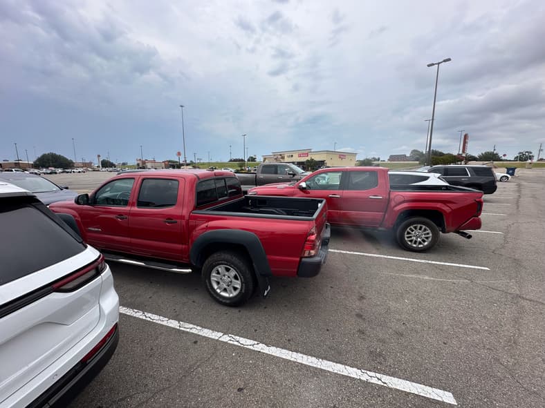 Two Generations Of Super Sonic Red Tacomas In A Parking Lot