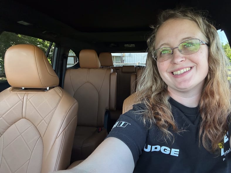 Driving the 2024 Toyota Highlander Hybrid Brought Pleasant Memories Back to the Surface 5 Erica Mueller Smiles In The Driver'S Seat Of The 2024 Toyota Highlander Hybrid With The Camera Pointed To The Very Rear