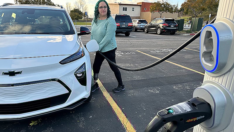 A Green-Haired, Amputee Woman Plugging In The Bolt Euv To Dc Fast Charge. Photo: Liv Leigh