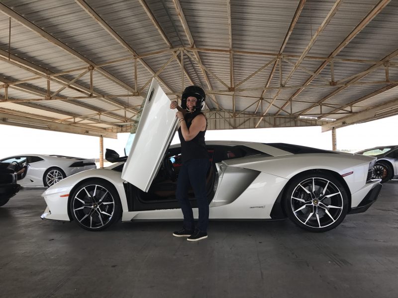 woman dressed in black with a black helmet in front of a white lamborghini