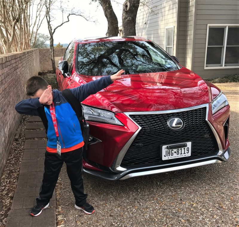 young boy dabbing in front of a red lexus sedan