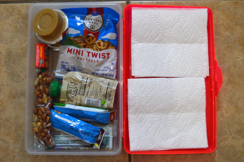 Assorted snacks that travel well for toddlers in a red and white container with napkins. 