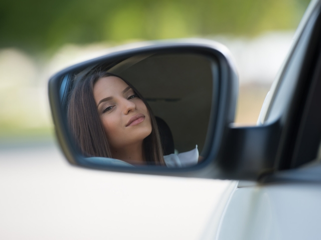 Woman's reflection in the sideview mirror of her sports car
