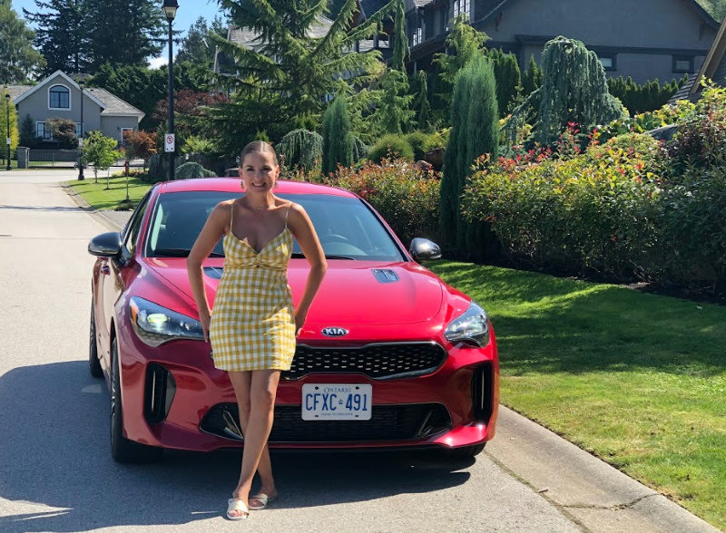 Woman in a yellow dress leaning on a red sports car