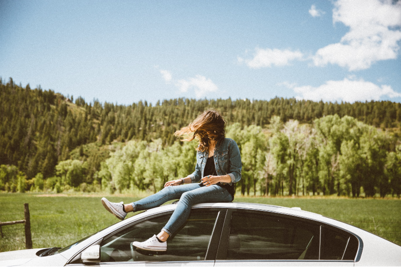 Girl sitting on top of her car, hair windblown