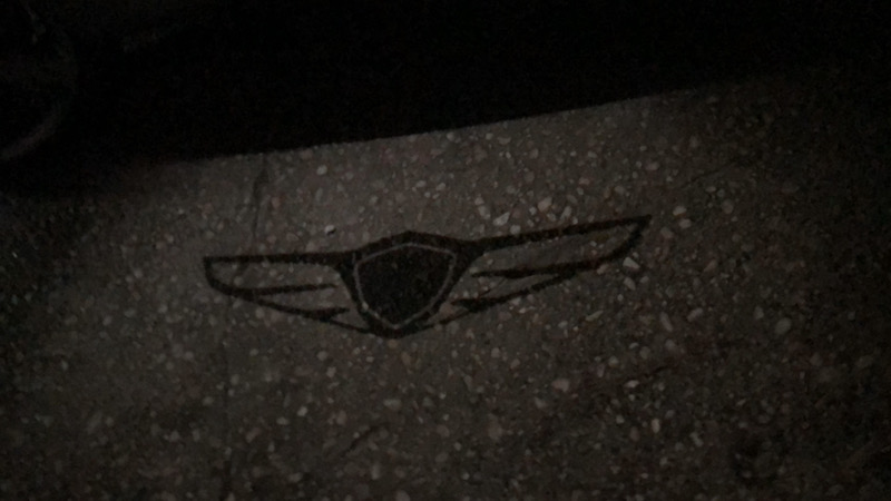 A puddle lamp lights up the pavement next to the driver's side door in the Genesis GV 80