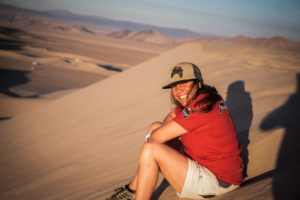 Nicole Sitting On A Sand Dune, Wearing Gear With Her Company