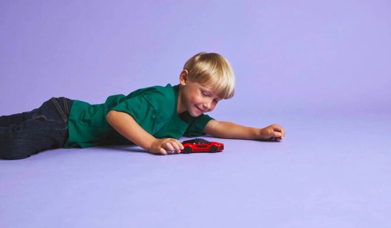 A Young Boy Playing With A Red Lego Sports Car Set